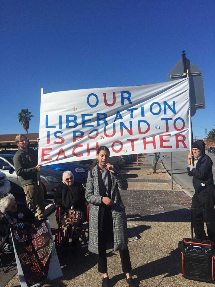 Protest speaker with banner which says "OUR LIBERATION IS BOUND TO EACH OTHER"