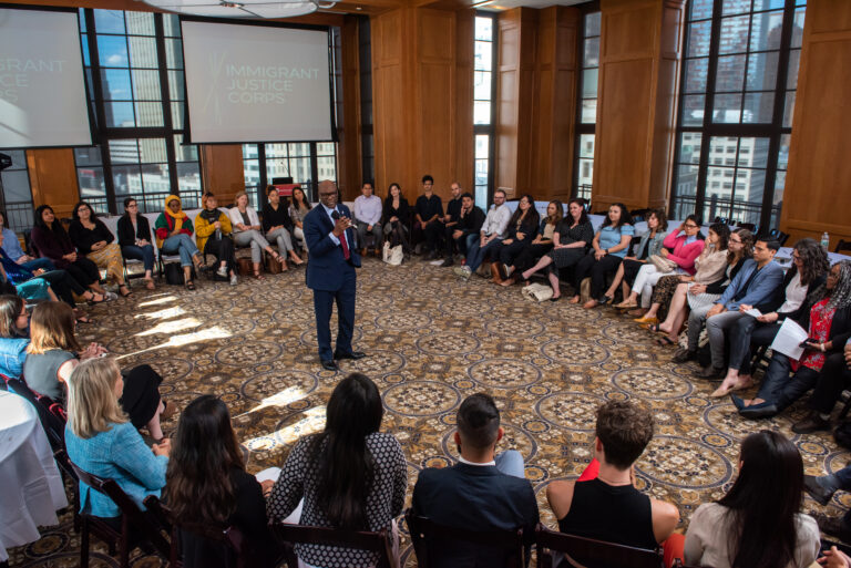 A group of people sitting in chairs around a man presenting with a microphone in the middle