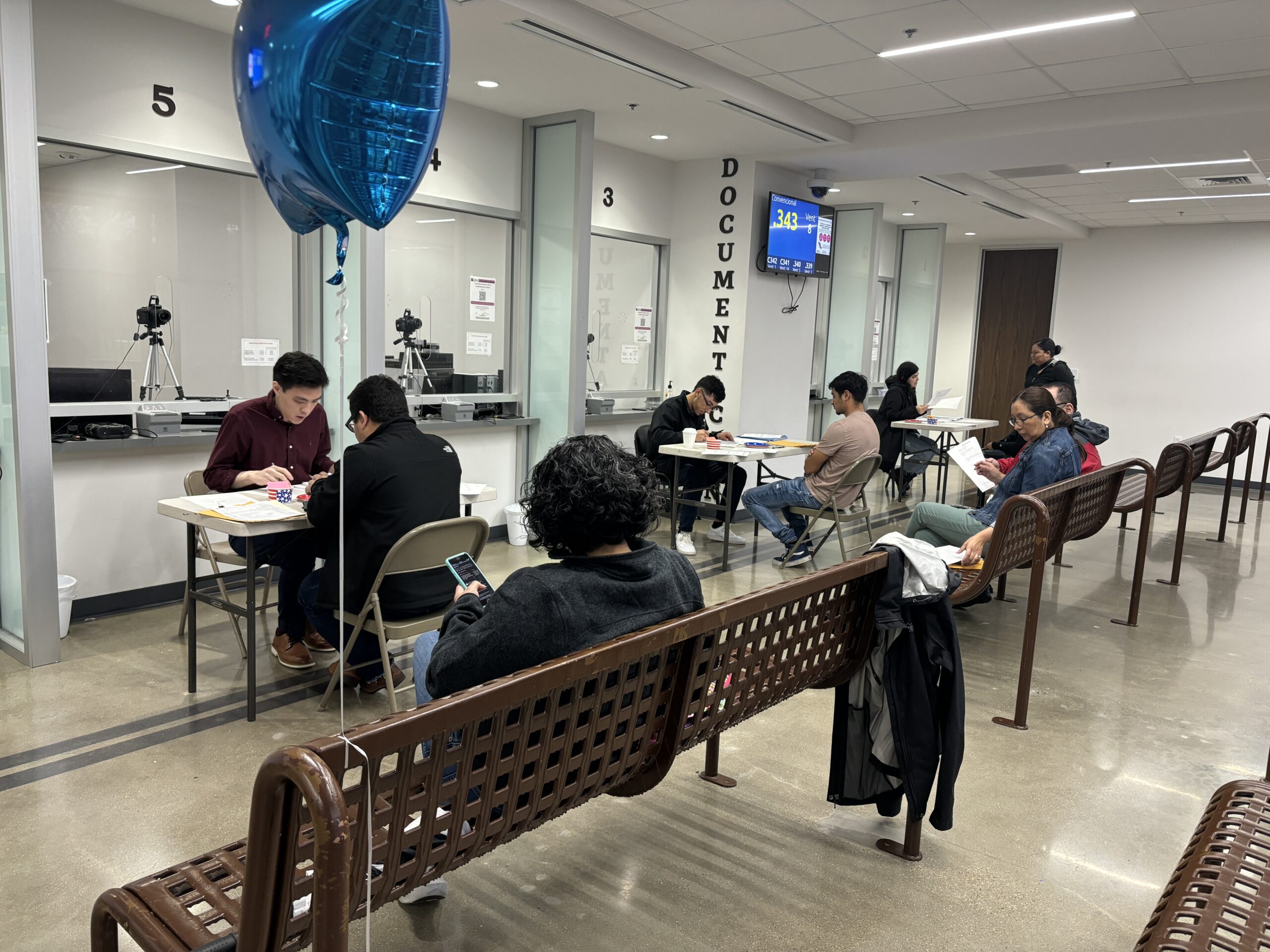 People waiting on benches before 3 desks with 2 people at each in front of booths