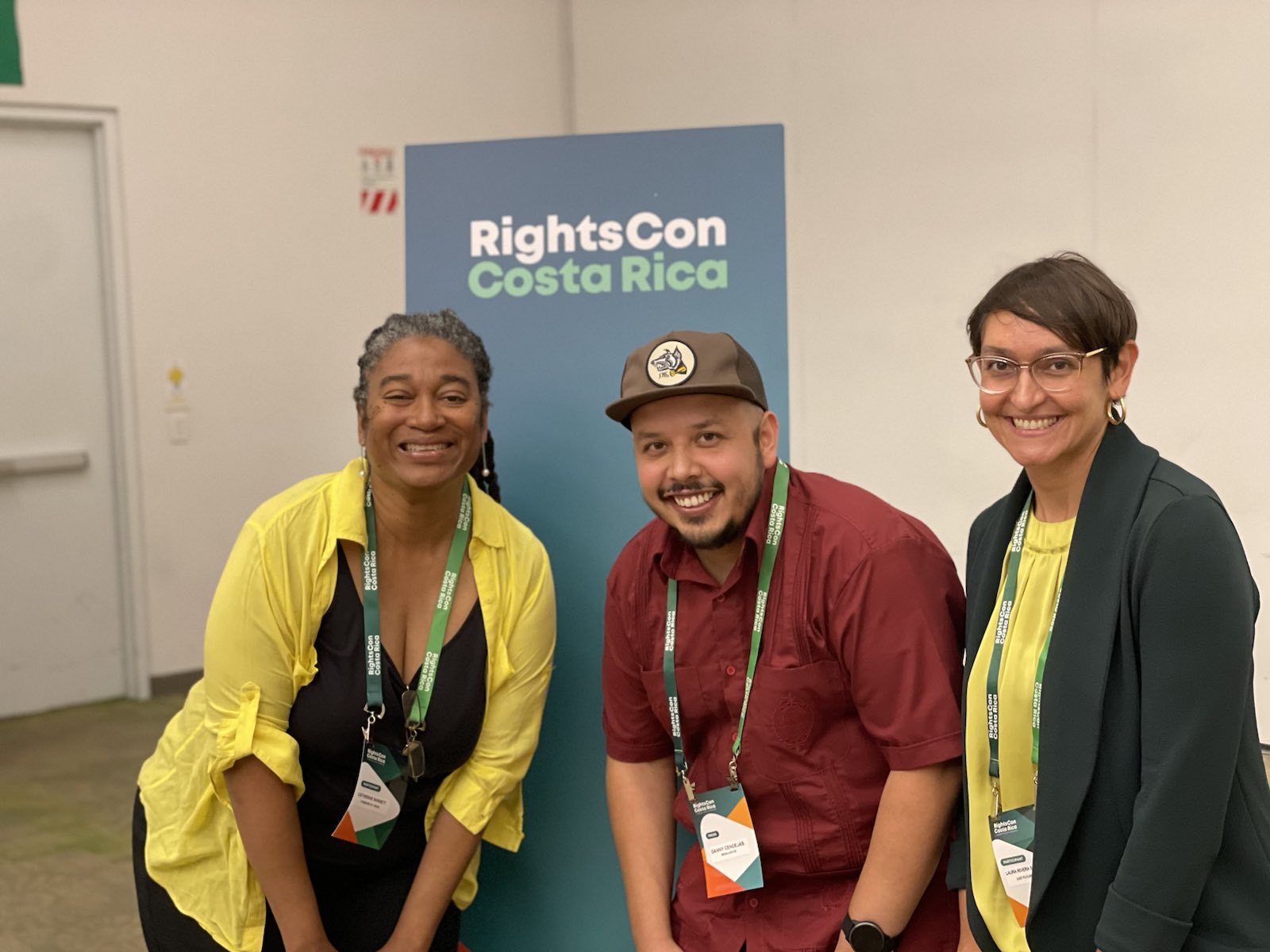 A group of three people in front of a blue sign that says "RightsCon CostaRica"