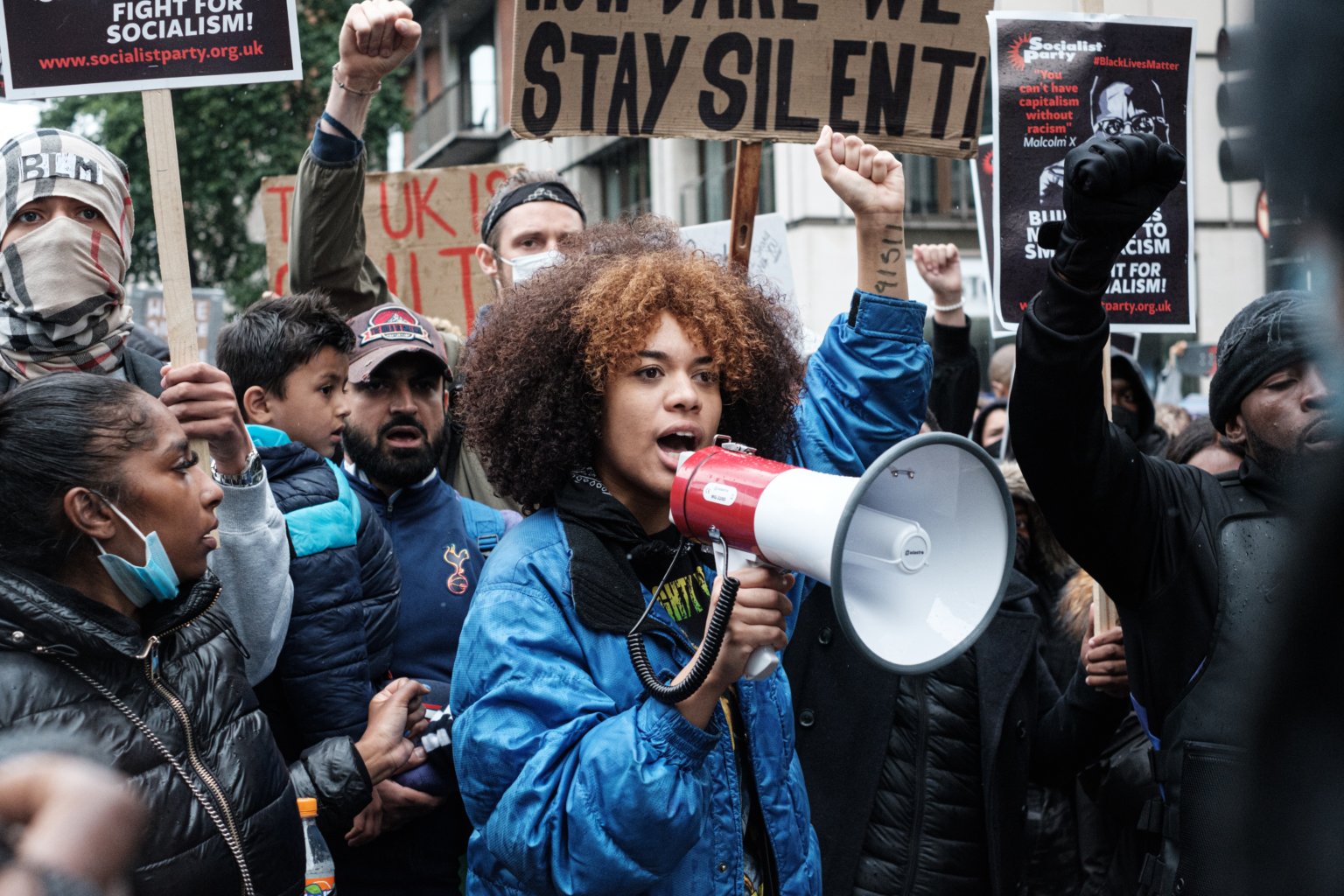 Woman with raised left fist and a megaphone with protestors behind her