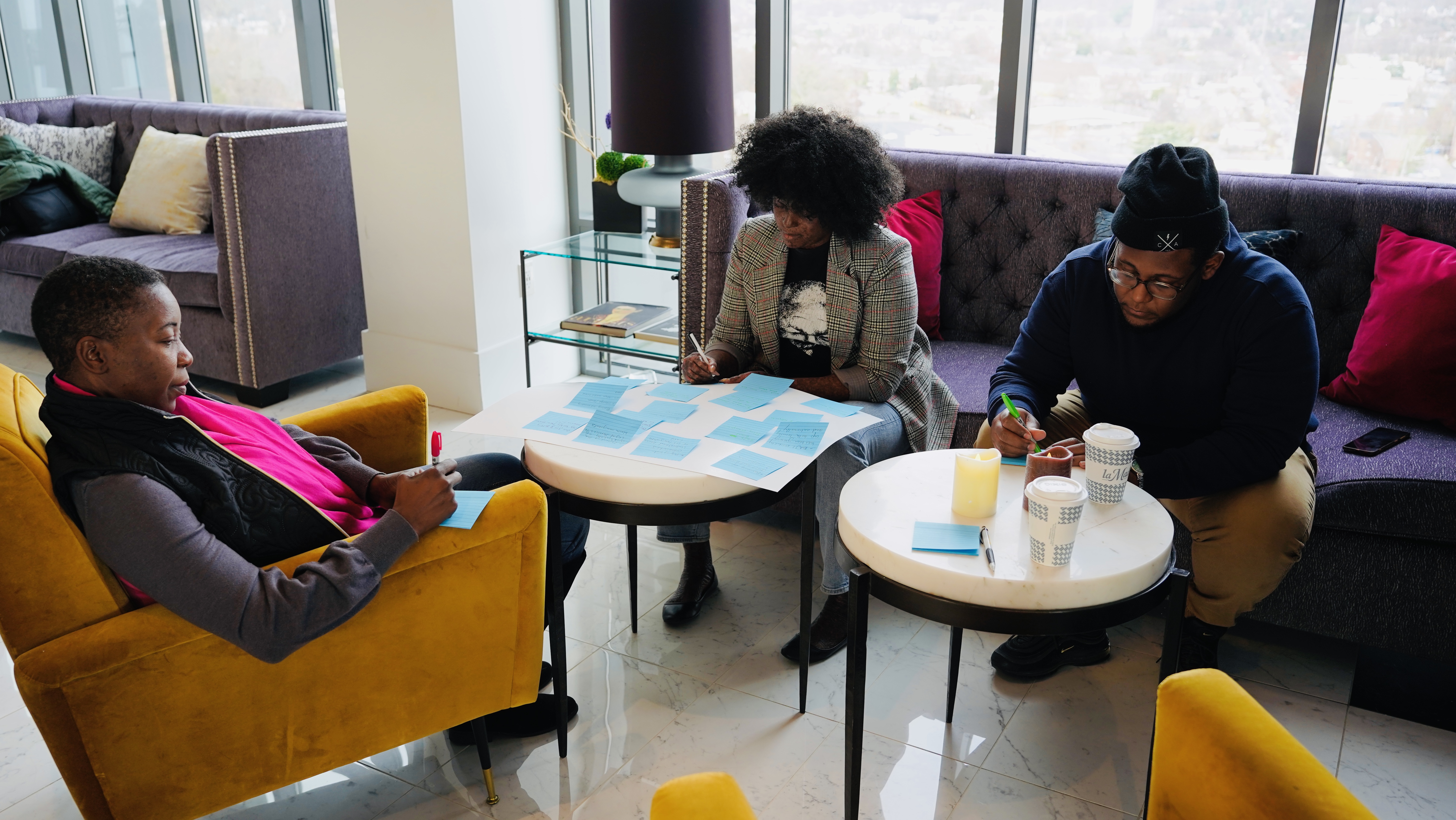 A group of 3 people sitting around tables on a couch and armchair over papers